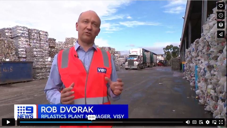 A man in a high visibility safety vest looking at the camera with bales of recycled plastic in the background