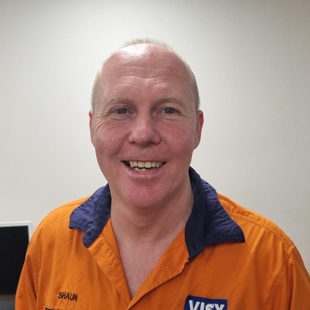 A man smiles at the camera, he is wearing an orange safety top with a Visy logo