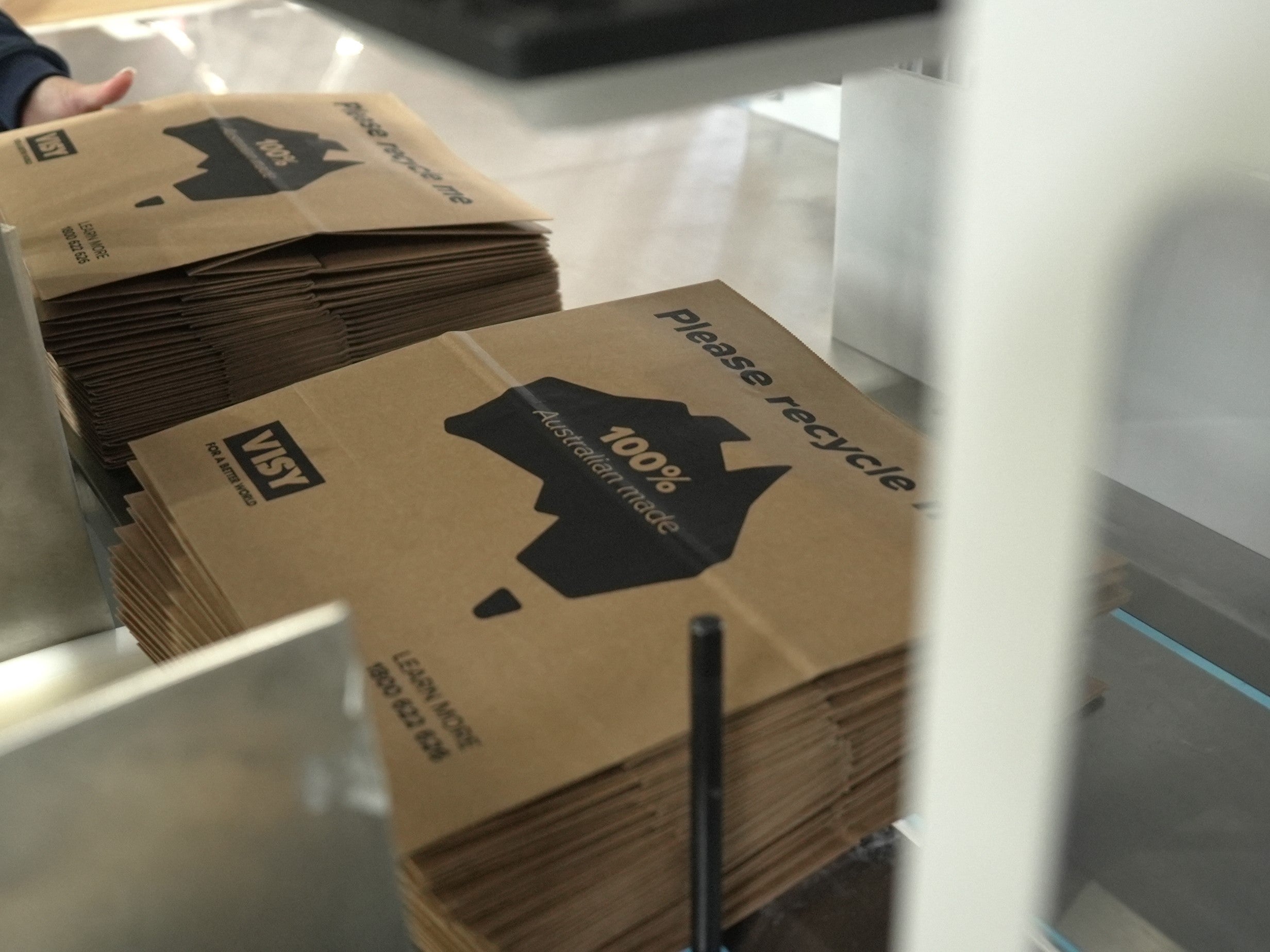 A stack of brown paper bags on a machine. The bag says 'please recycled, 100% Australian made'.