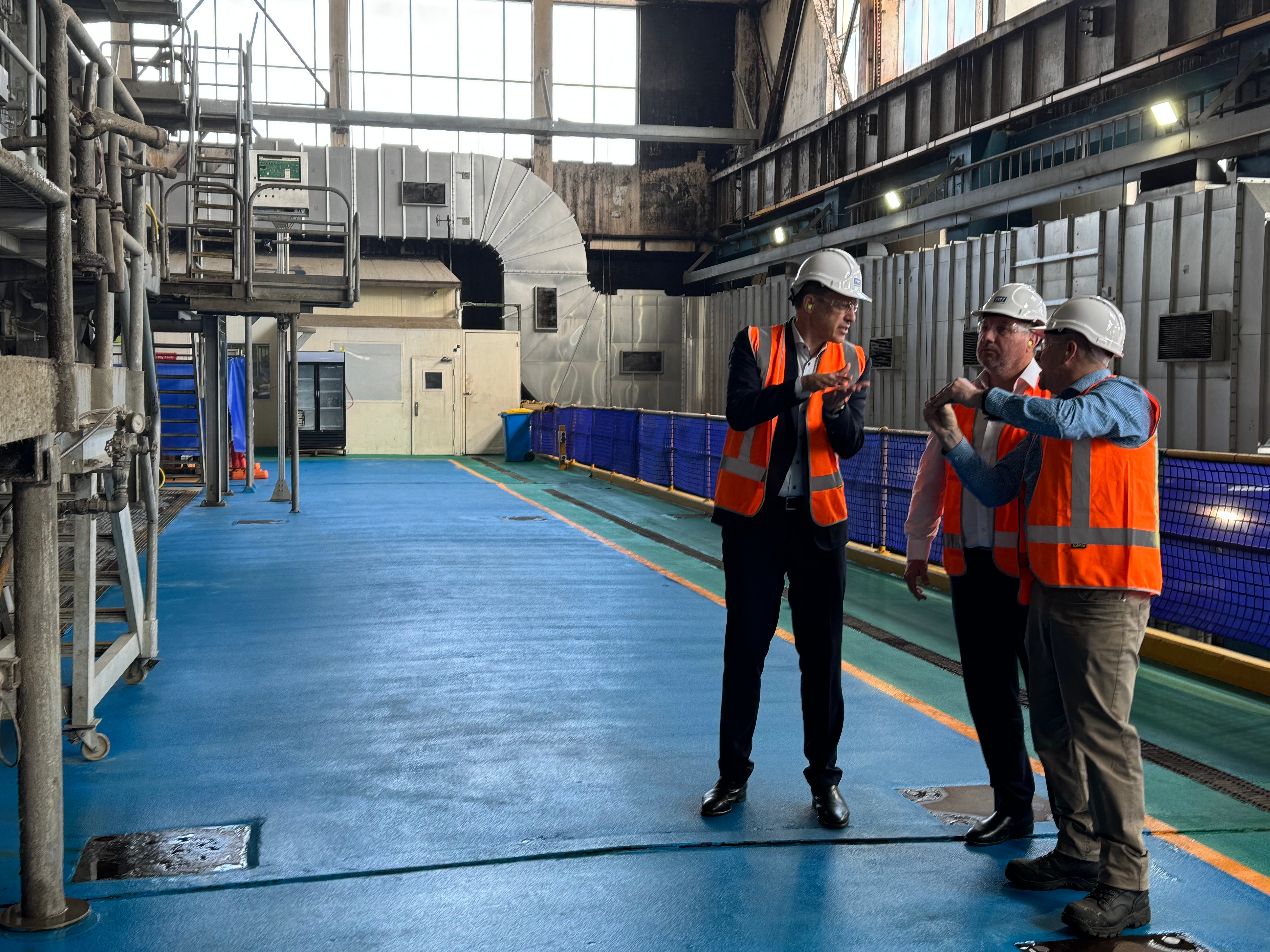 Three men in high vis and safety work wear are talking to each other in an industrial building