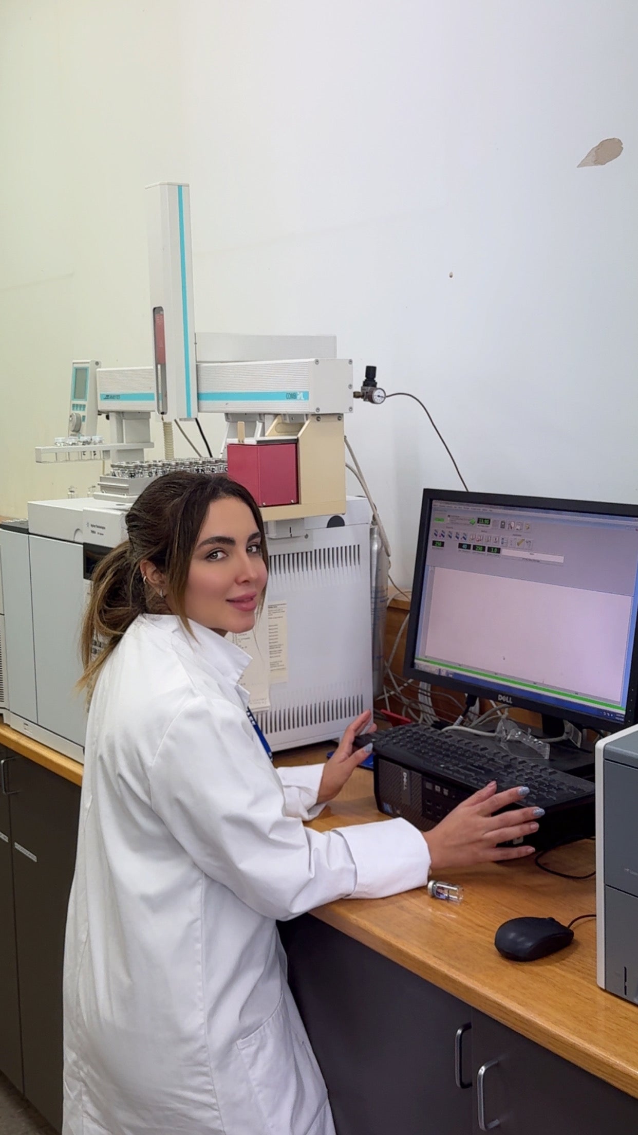 Woman in white lab coat smiles while working at her desk.