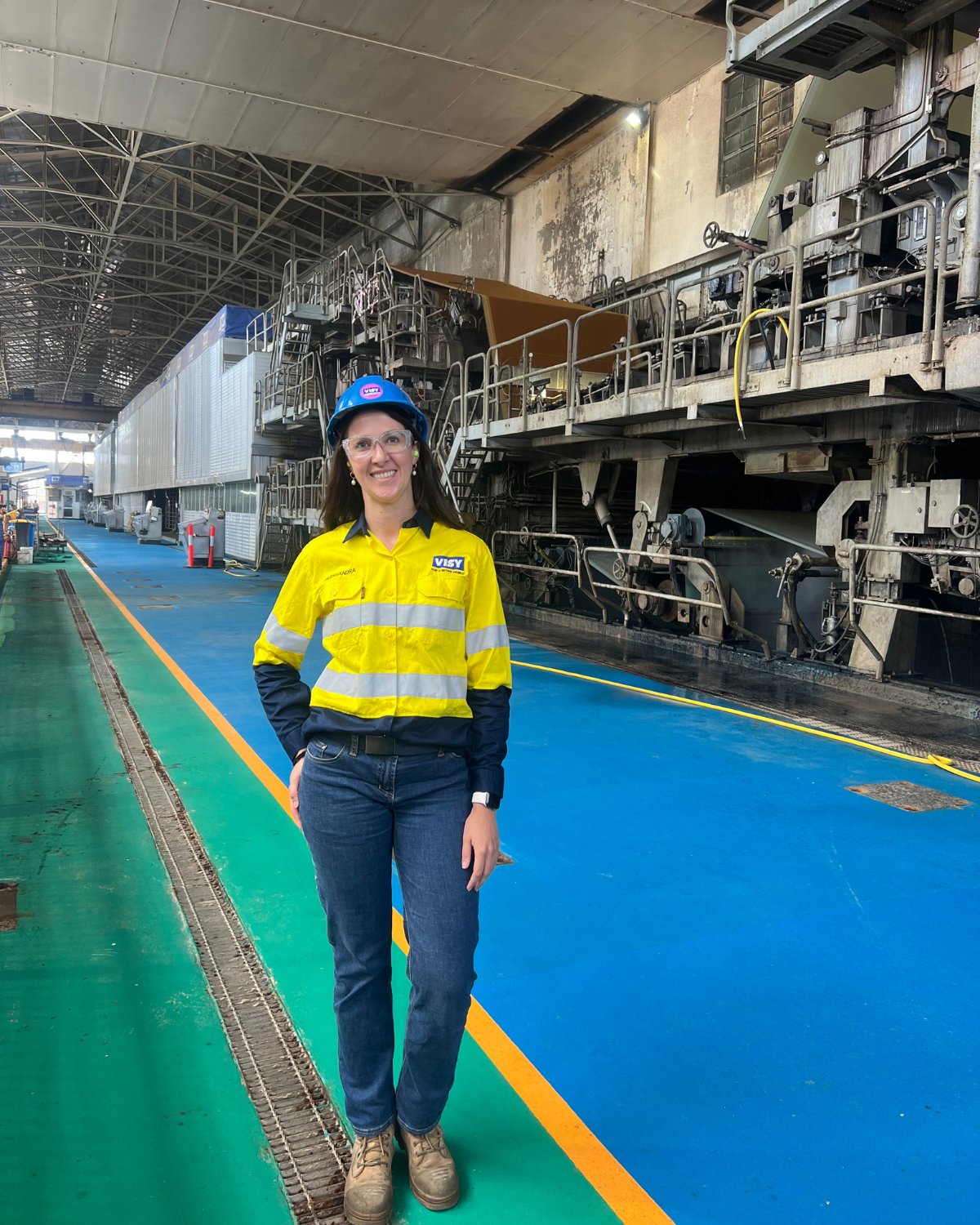 Woman in high-vis top and pants smiles in front of Visy's Gibson Island paper mill.