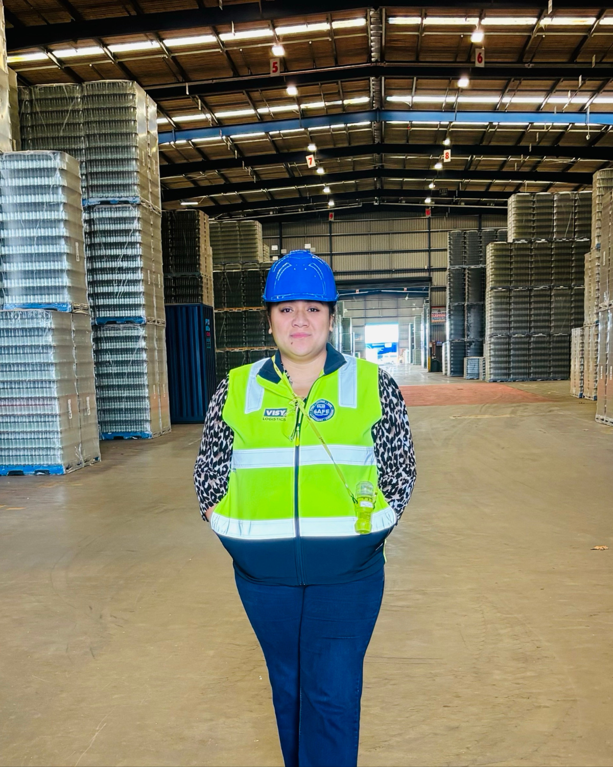 Woman in yellow high-vis vest and hard hat stands in Visy warehouse space.