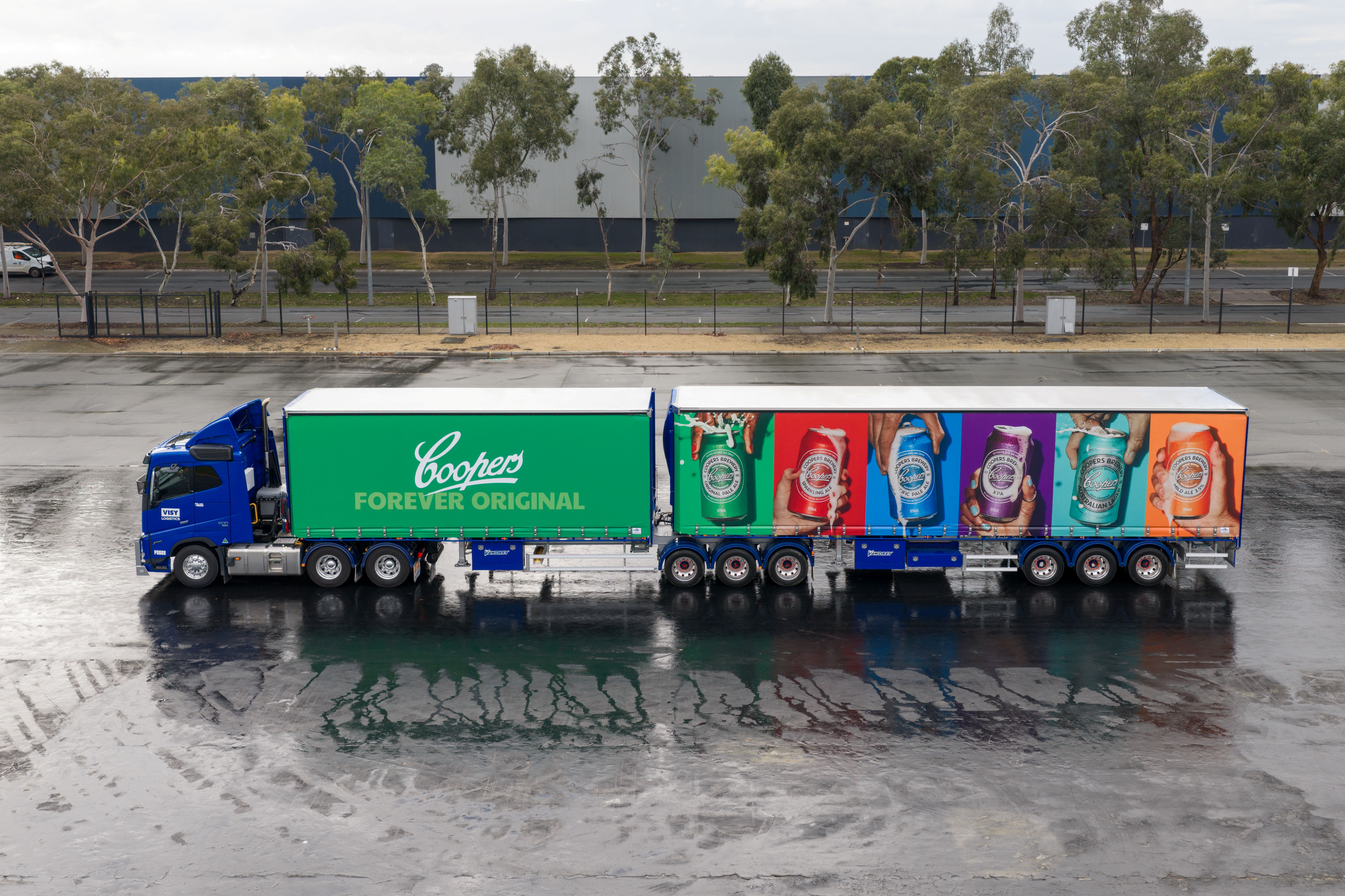 Visy Logistics truck with bright Coopers Brewery branding on the livery. Trees and warehouse in background