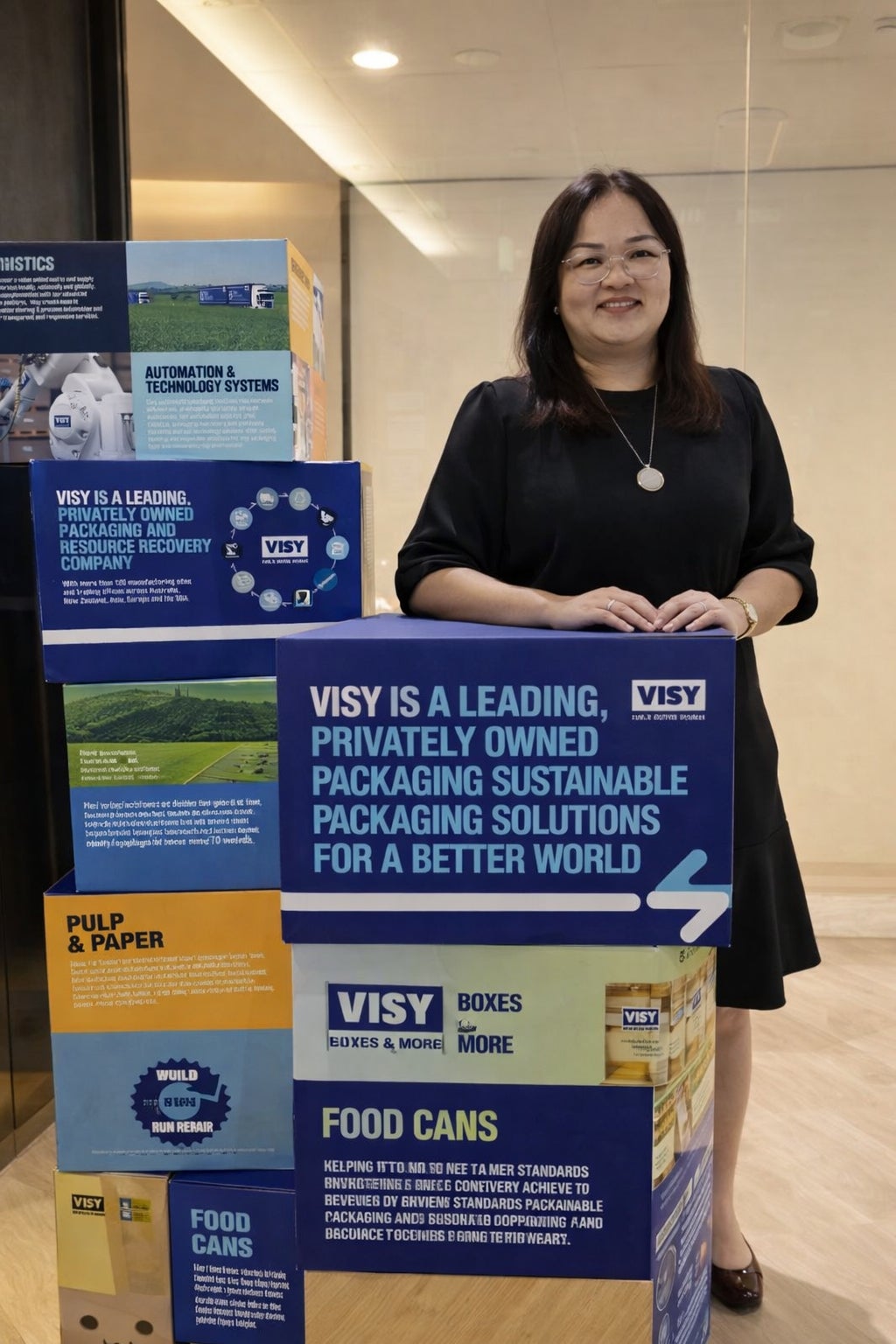 Pearl wears a black dress and smiles at the camera while posing next to Visy signage