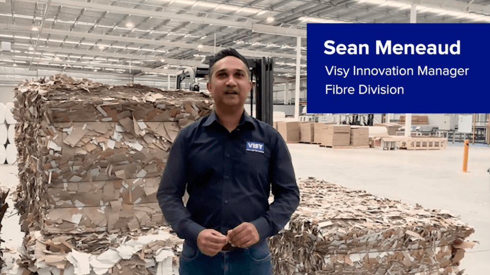 A man wearing a blue shirt standing in front of bales of shredded cardboard. 