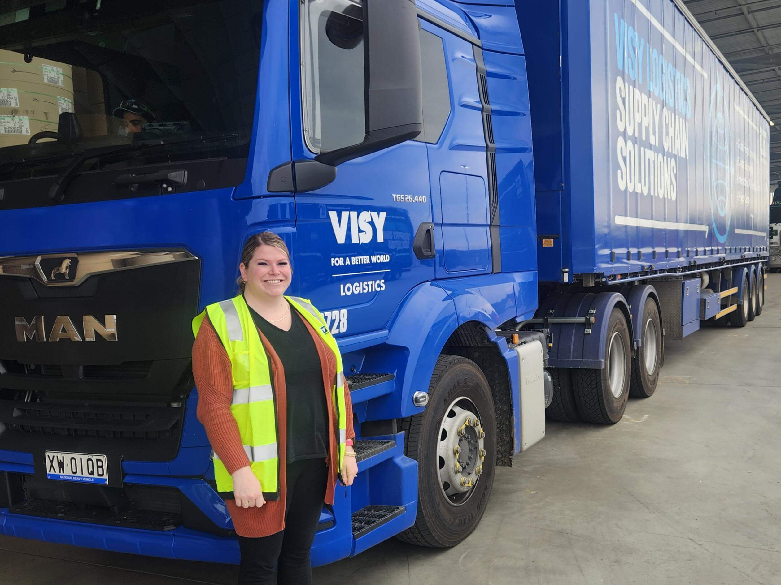 Woman standing in front of blue truck in yellow hi-vis 