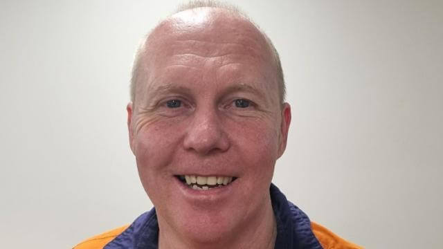 A man smiles at the camera, he is wearing an orange safety top with a Visy logo