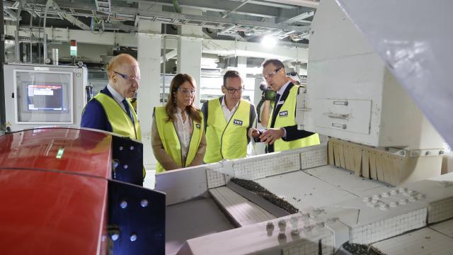 Four people in high visibility yellow safety vests are looking at a glass sorting machine