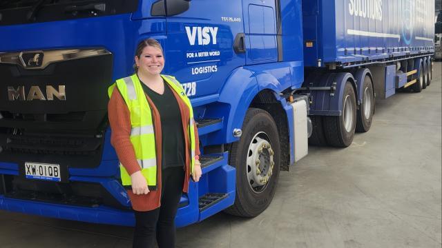 Woman standing in front of blue truck in yellow hi-vis 