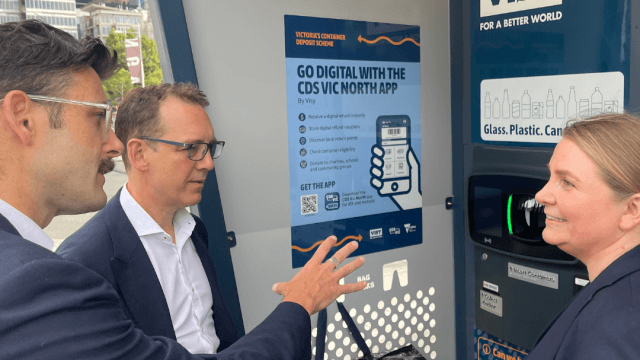 Two men and a woman are talking in front of a blue reverse vending mahcine