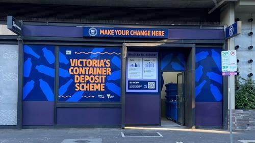 Image of The District Docklands Reverse Vending Machine shop front, in Victoria's Container Deposit Scheme branding of Blue and Orange