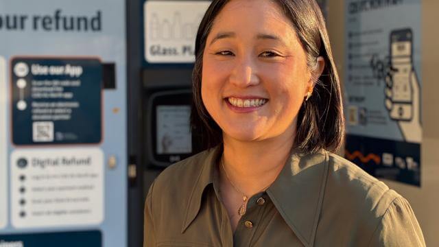 A woman in khaki shirt smiles at camera, she is standing in front of a blue machine