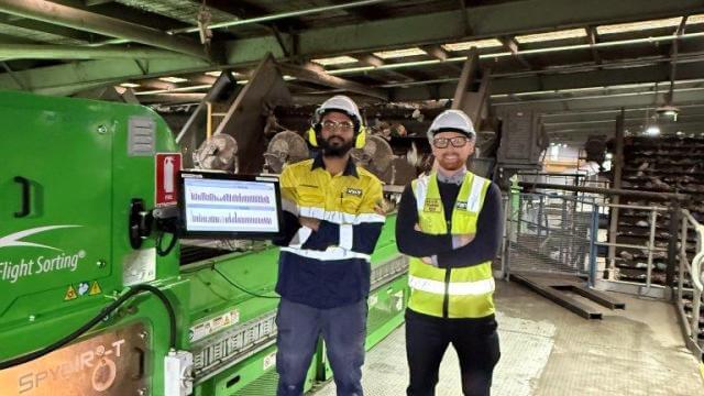 Two men in high visibility safety wear are smiling at the camera with arms folded, they are in a warehouse with equipment behind them