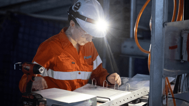 Construction team member wearing PPE and a head lamp reads from a binder.