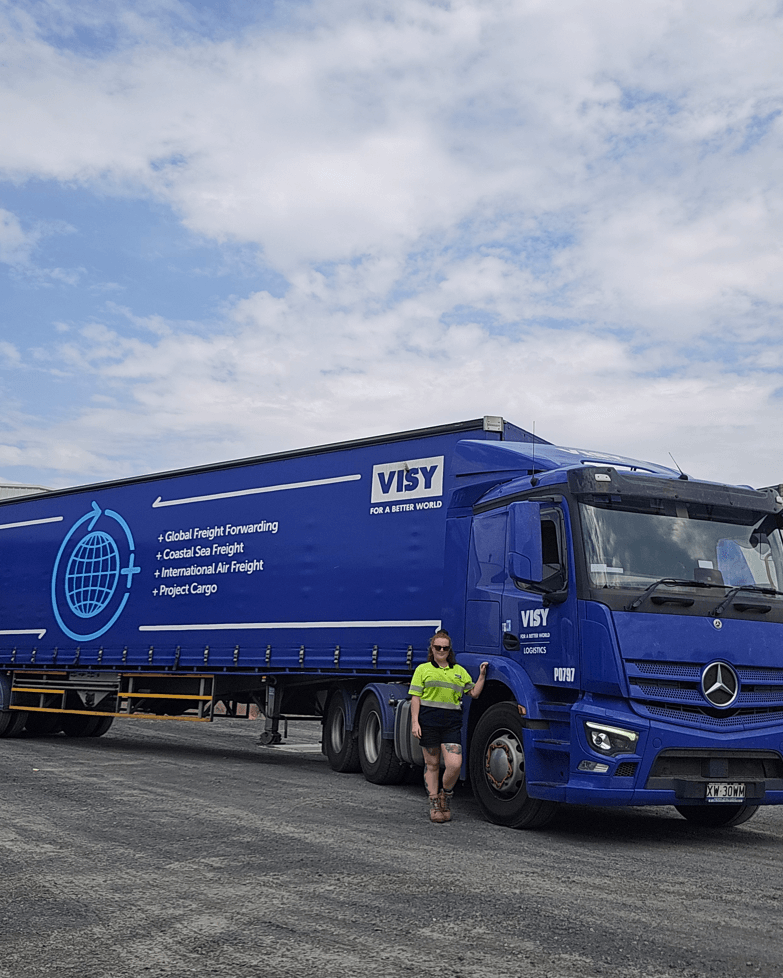 Woman in high-vis top and shorts smiles next to a Visy Logistics truck.