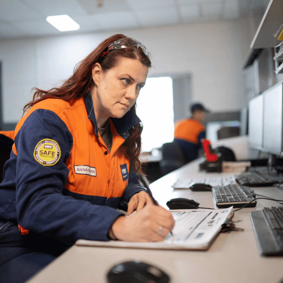 Woman in high-vis takes notes while looking at her computer.
