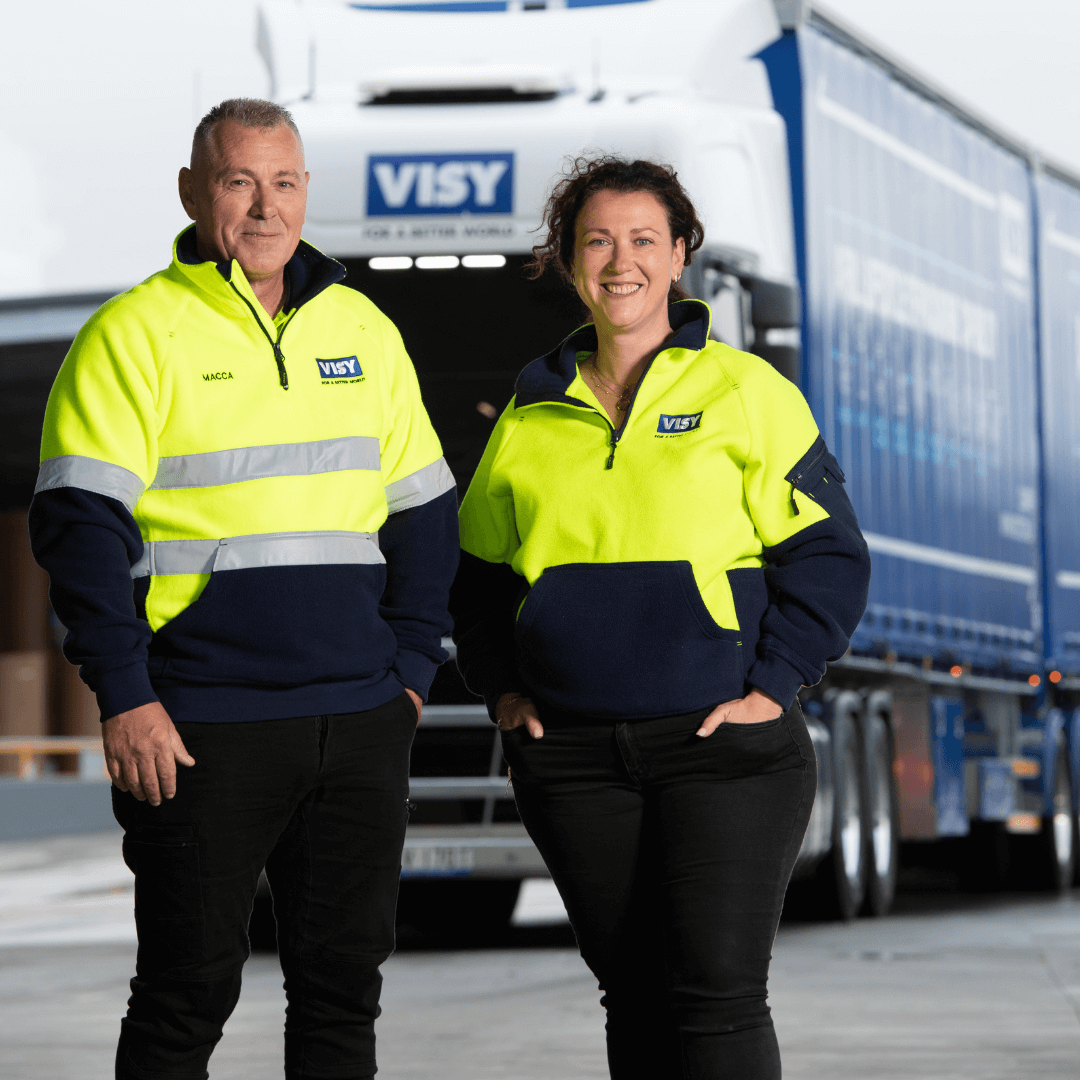 Man and woman in high-vis stand in front of a Visy Logistics truck and smile.