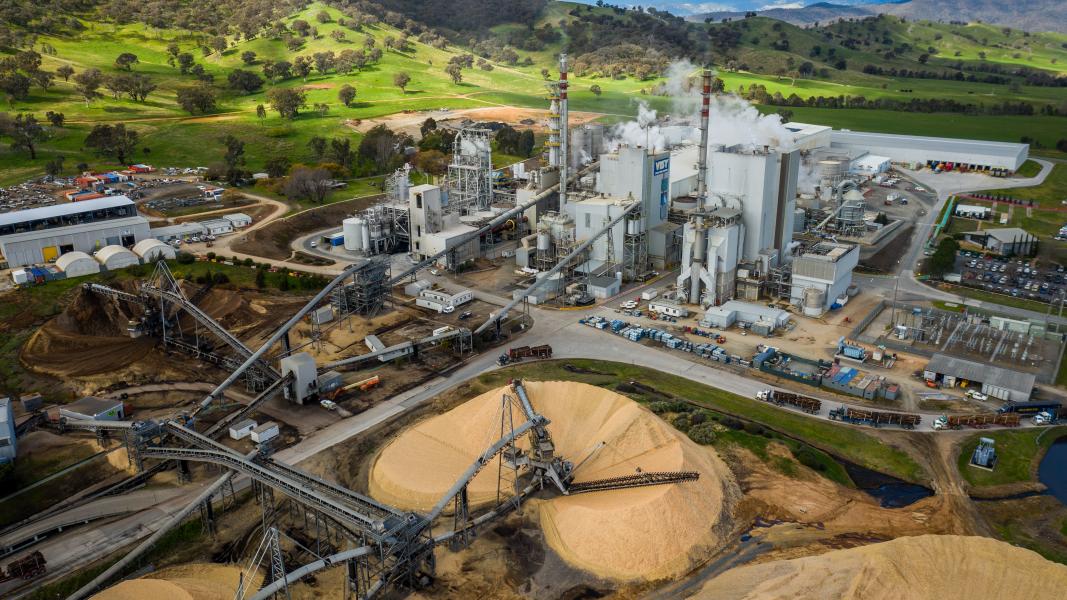 An industrial looking paper mill set amongst green countryside with stacks of wood chips