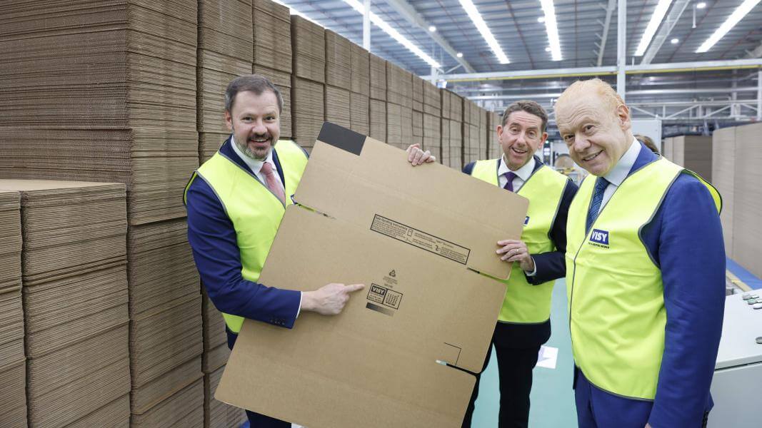 Three men holding up flat cardboard box