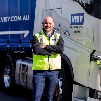 A man in a high visibility safety vest smiles at a camera in front of a Visy truck