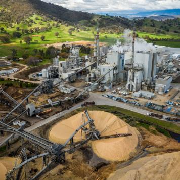 An industrial looking paper mill set amongst green countryside with stacks of wood chips