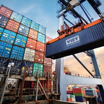 A Visy branded shipping container is being lifted by machinery with lots of other shipping containers in background