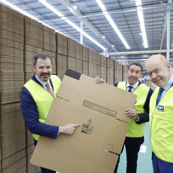 Three men holding up flat cardboard box