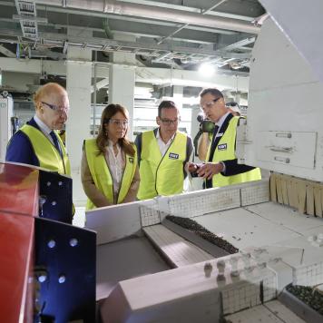 Four people in high visibility yellow safety vests are looking at a glass sorting machine