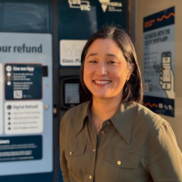 A woman in khaki shirt smiles at camera, she is standing in front of a blue machine