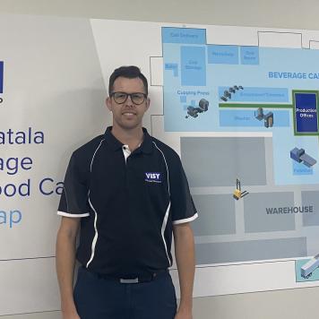 A man smiles at camera in navy blue clothes, he is standing in front of a site map for Visy Yatala beverage and food can