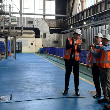 Three men in high vis and safety work wear are talking to each other in an industrial building
