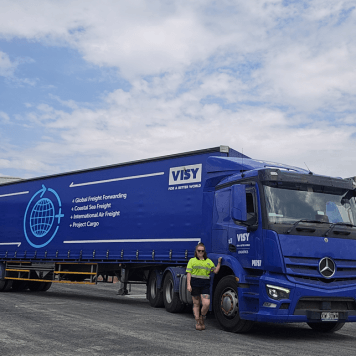 Woman in high-vis top and shorts smiles next to a Visy Logistics truck.