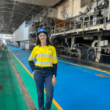 Woman in high-vis top and pants smiles in front of Visy's Gibson Island paper mill.
