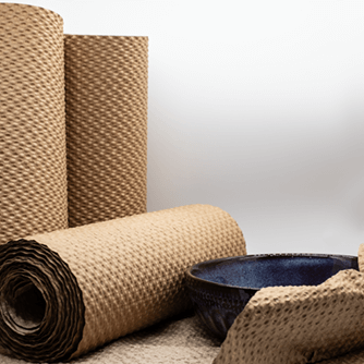 Rolls of brown paper bubble wrap are stacked up and lying down, a black kitchen bowl is half wrapped in it