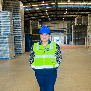 Woman in yellow high-vis vest and hard hat stands in Visy warehouse space.