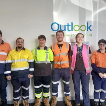 Six people stand in a line smiling at the camera. They are all wear hi-visibility work clothes.