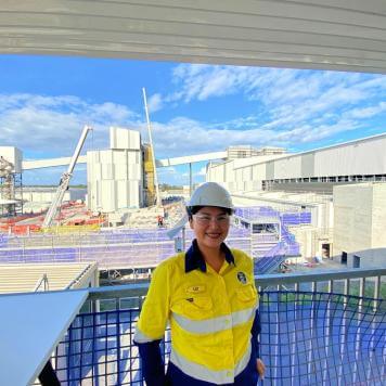Liz, wearing yellow high-vis, safety goggles and hard hat, smiles in front of construction at Visy Glass Yatala.