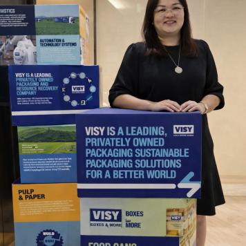 Pearl wears a black dress and smiles at the camera while posing next to Visy signage